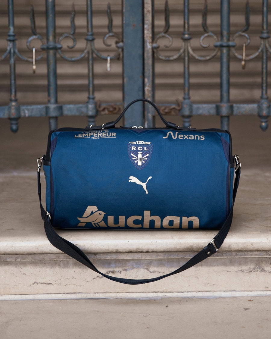 Sac 45 taillé dans le maillot Sainte-Barbe 2025/26 du RC Lens, bleu, posé sur des marches au Louvre