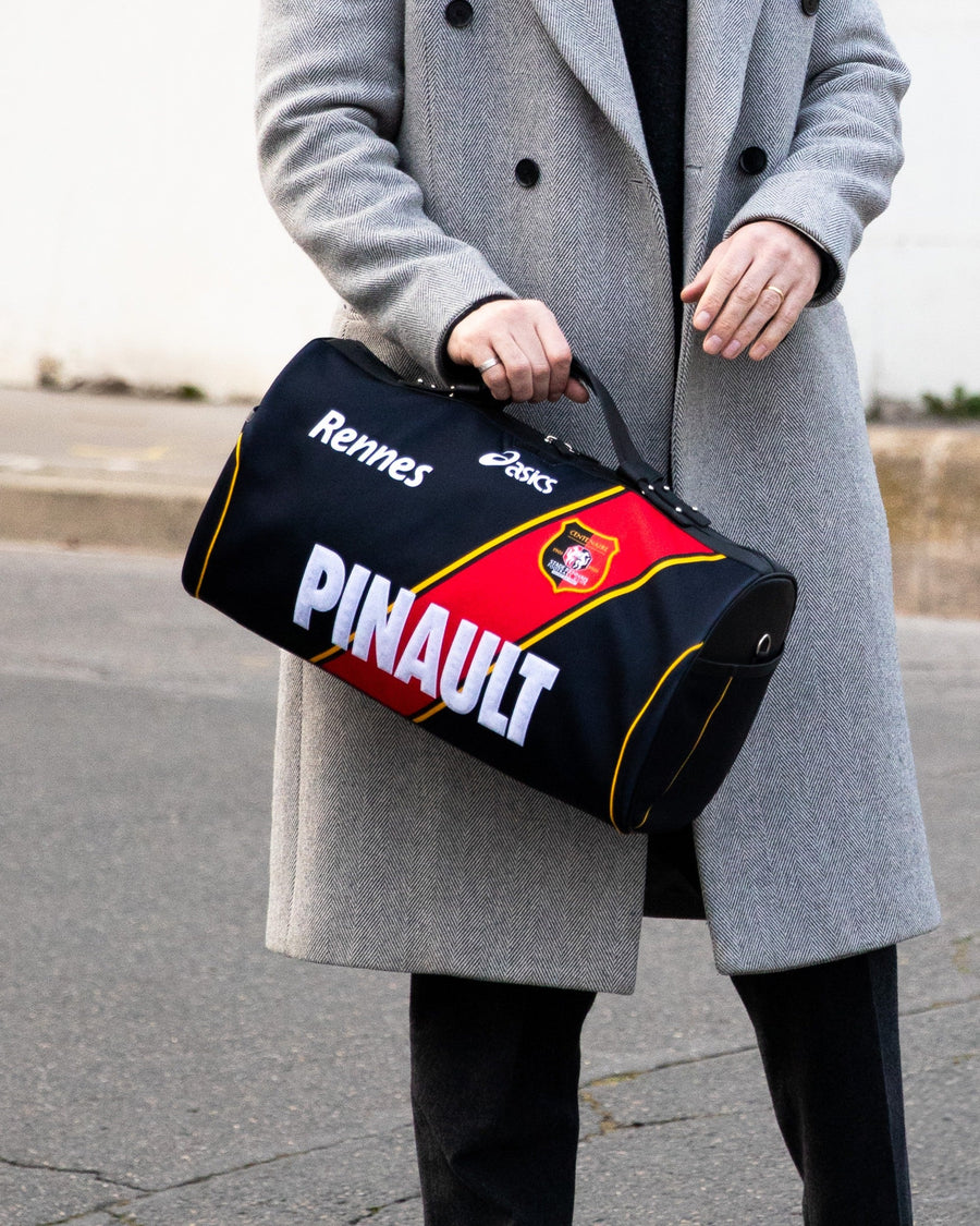 Sac JOUBERT en maillot du Stade Rennais, noir à diagonale rouge, sponsor Pinault, tenu à deux mains