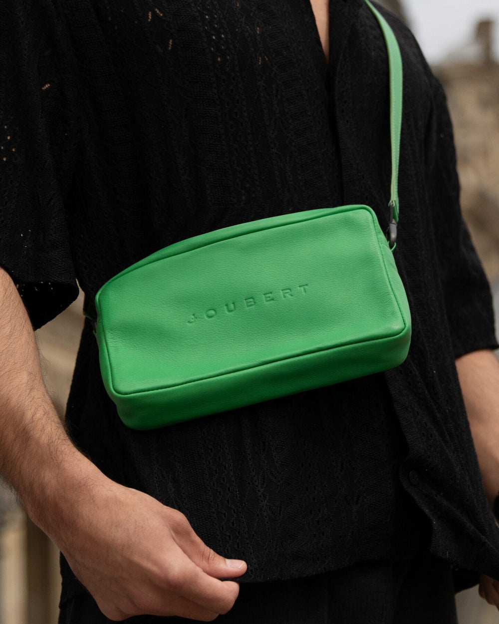 Green calfskin Joujou bag worn across the body in front of the Louvre pyramid.