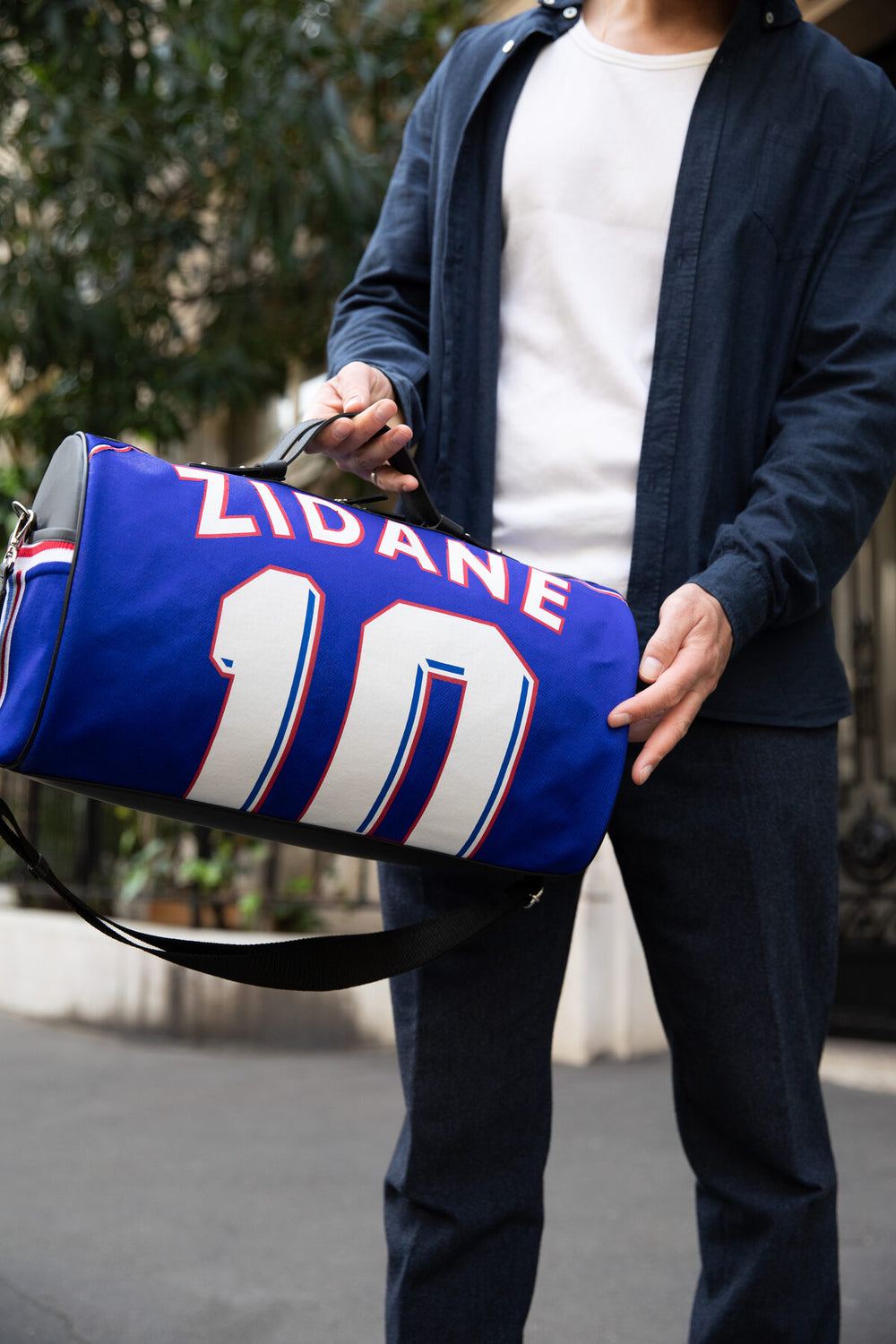 Cylindrical Métamorphose bag made from a 1998 France national team jersey, carried by hand on a Paris street.